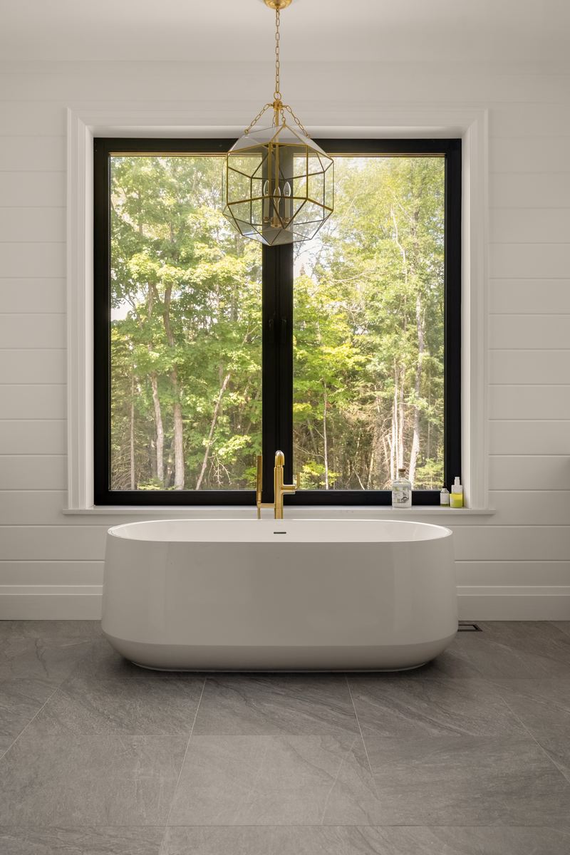 Primary ensuite freestanding soaker tub under a tall black-framed window