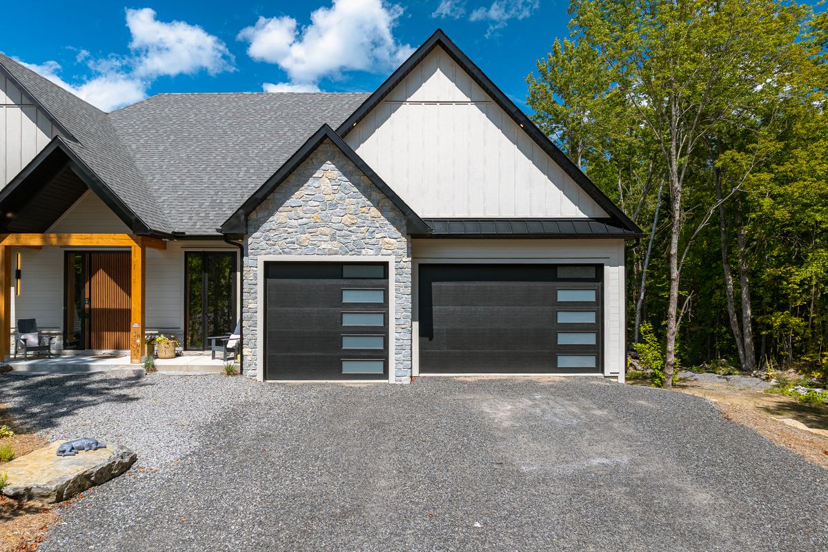 Front exterior of 11 Glen Eagle Court, stone and board-and-batten with two black garage doors