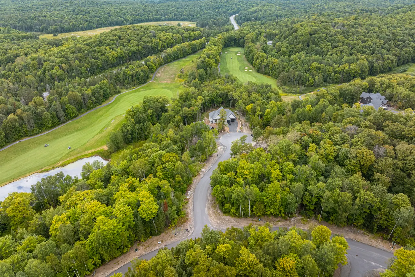 Aerial view of Glen Eagle Court winding up past treed lots to finished homes at Deerhurst Highlands, with fairways behind