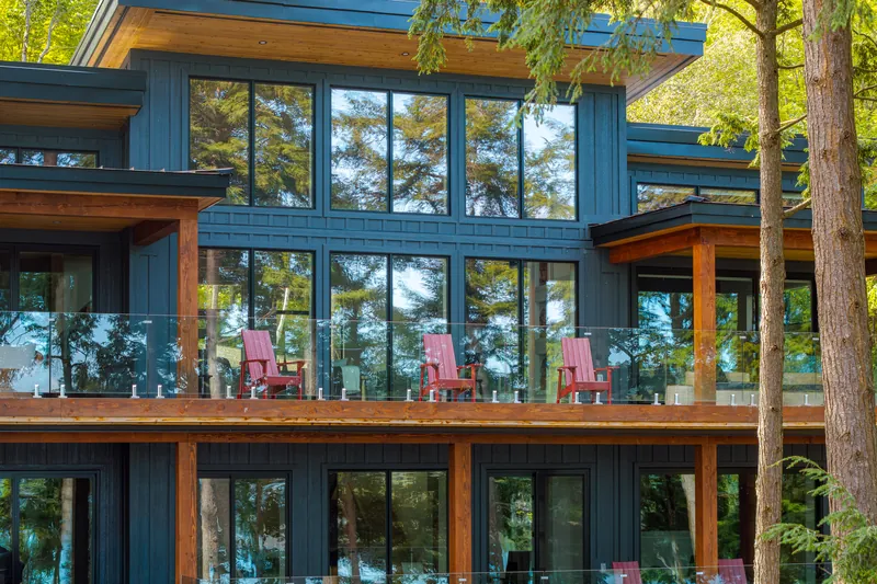 Lakeside elevation of Hemlock Point in dark board-and-batten with floor-to-ceiling windows, cedar posts and a glass-railed deck