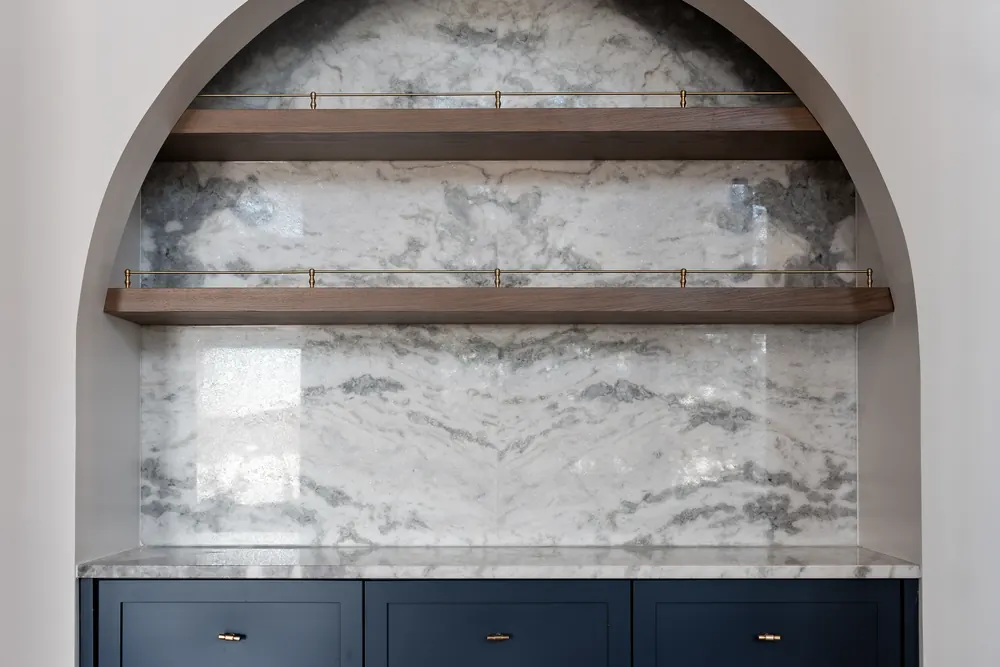 Servery at Hemlock Point set in an arched niche, with marble backsplash, walnut shelves and navy cabinetry